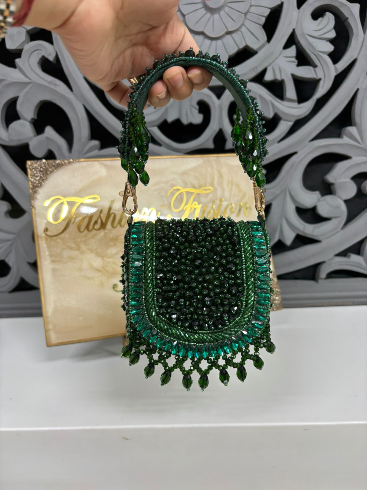 Green beaded handbag held by a hand with a decorative background