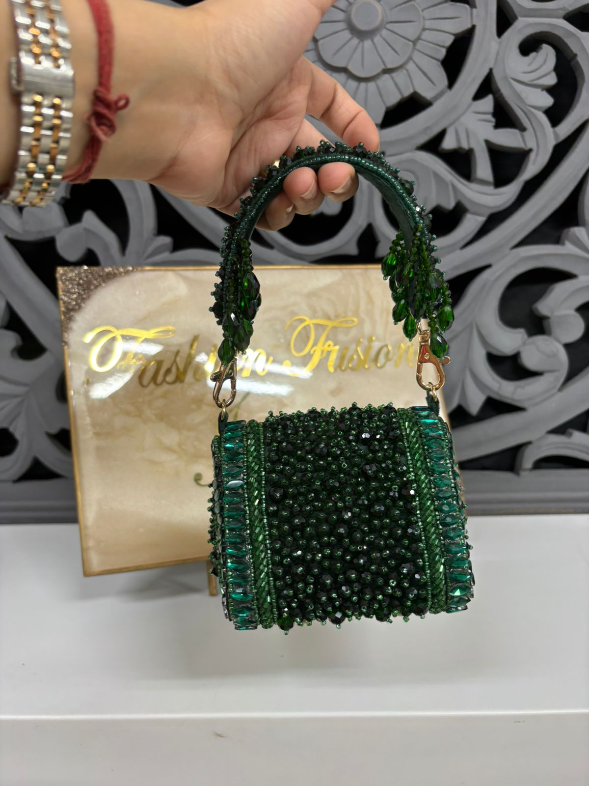Green beaded handbag held by a hand with a decorative background