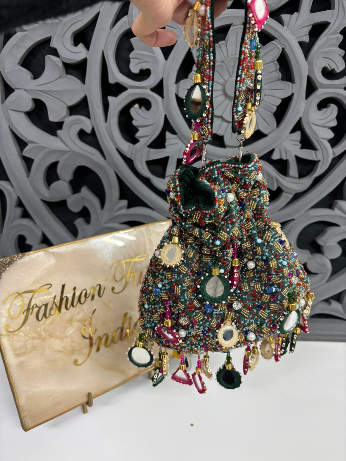 Beaded handbag with colorful details on a stand, against a decorative wall.