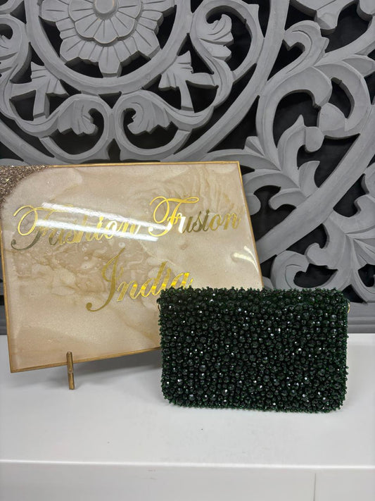 Dark Green beaded clutch bag next to a decorative plaque with gold text on a white surface.