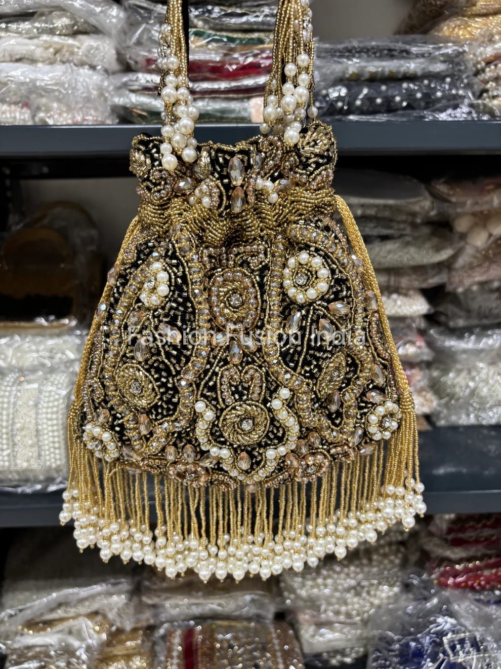 Decorative handbag with gold and black embroidery and pearl details on a blurred background.