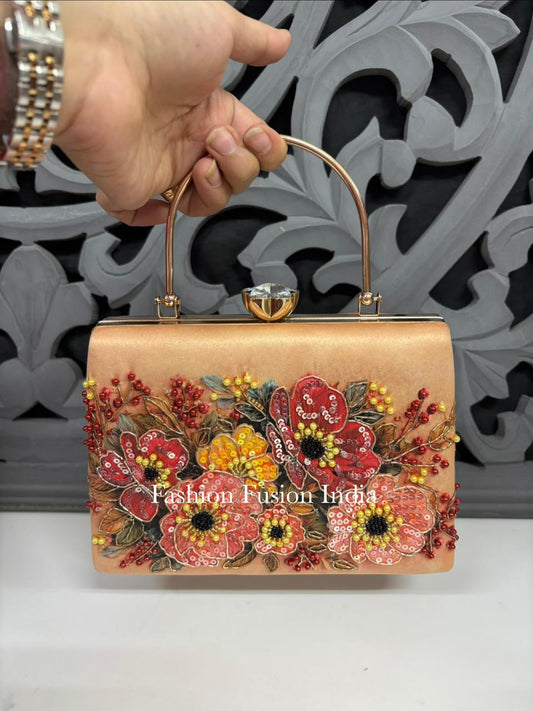 A peach-colored leather clutch handbag with a gold-tone metal top handle and clasp, decorated with 3D floral embroidery in red, pink, yellow, and green. 