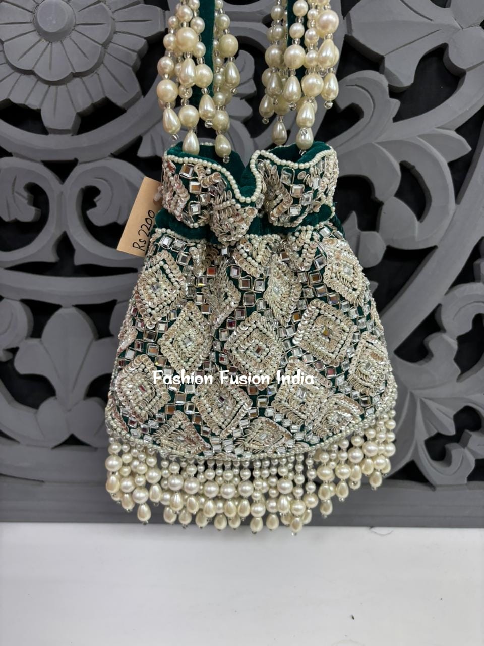 Decorative handbag with pearls and intricate design on a white surface with a decorative gray background.