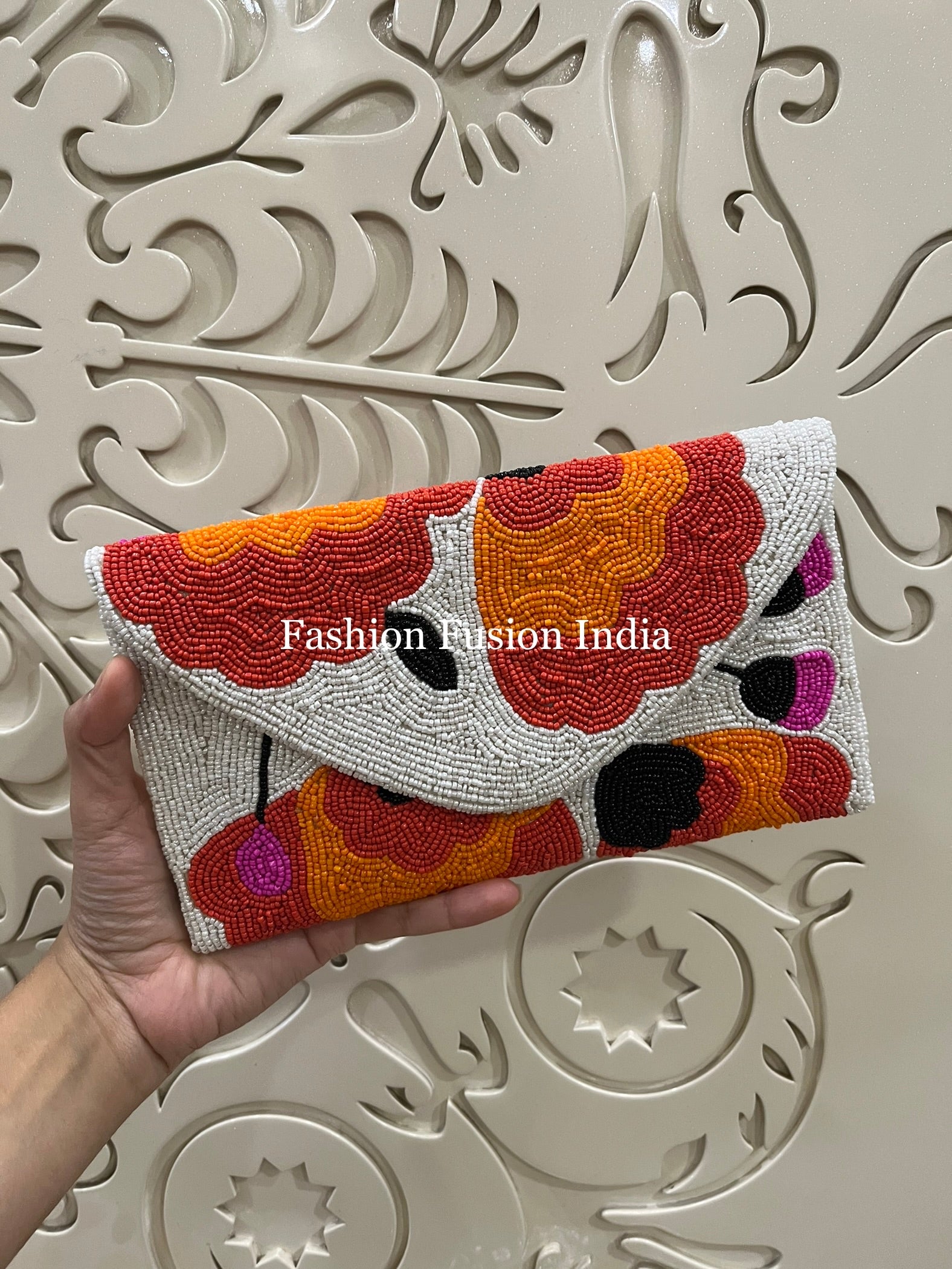 A hand holding a multicolor beaded flap bag against an ornate background.