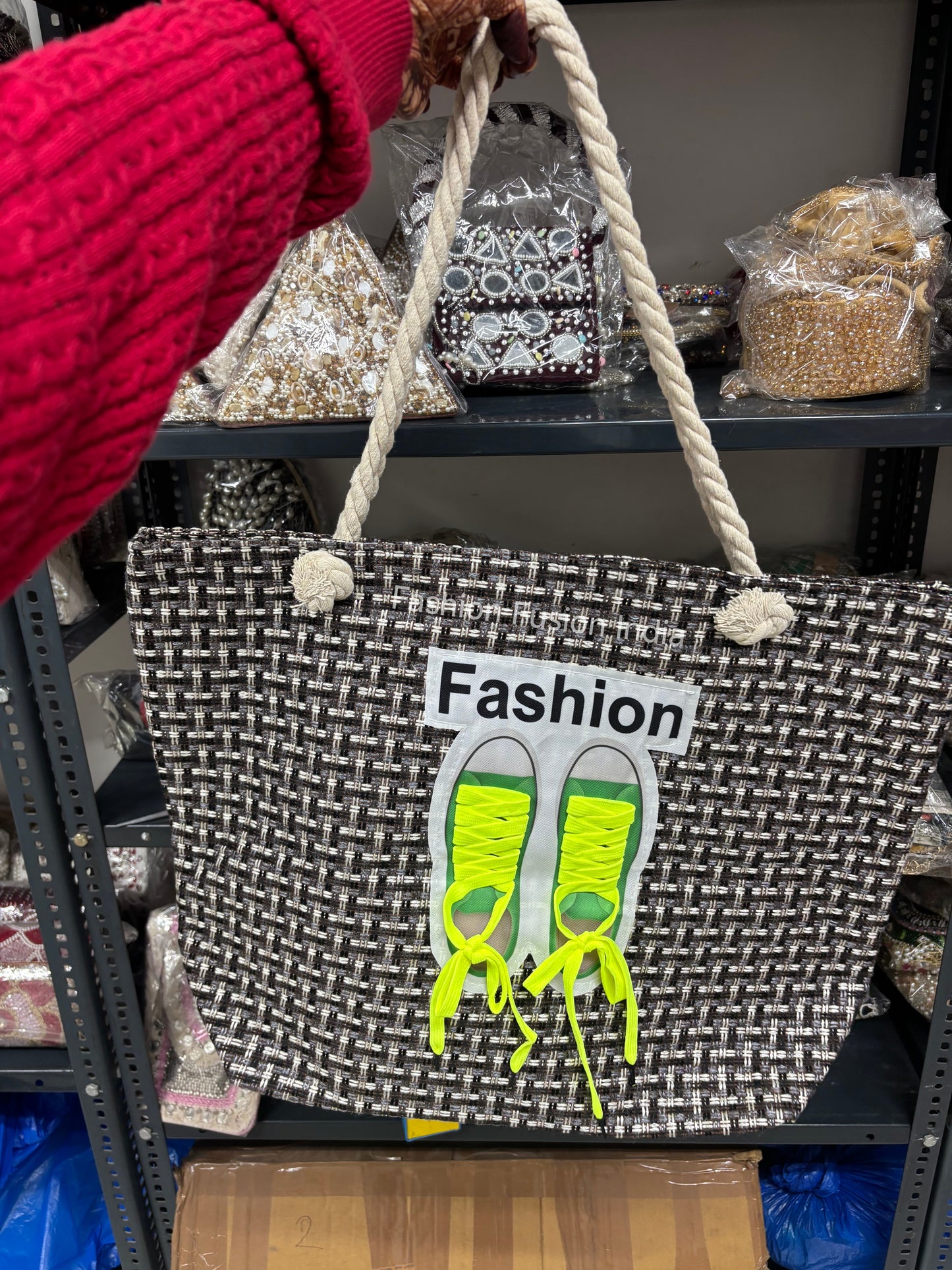 Black and white woven bag with green shoes design and 'Fashion' text, held by a person wearing a red sleeve.