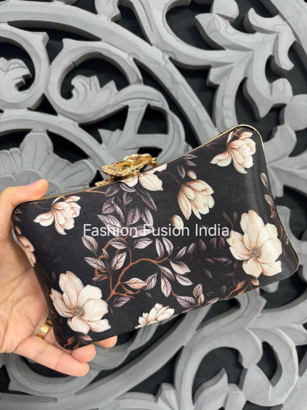 Floral-patterned clutch held by a hand with 'Fashion Fusion India' branding against an ornate background.