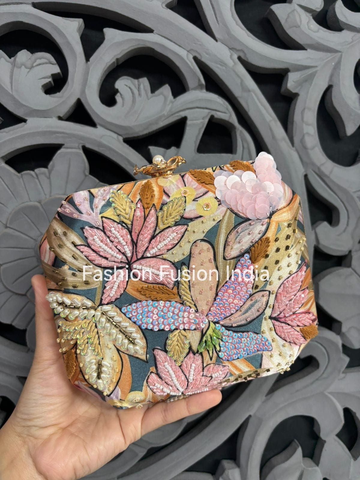 Floral patterned clutch held by a hand against an ornate background