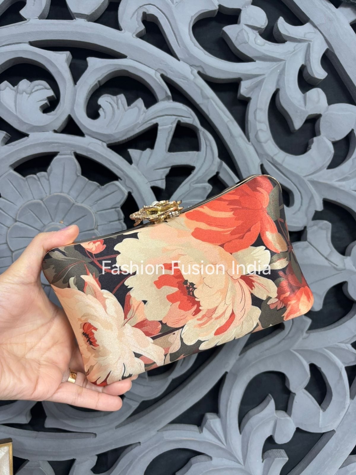 Floral clutch held by a hand against an ornate black and gray background