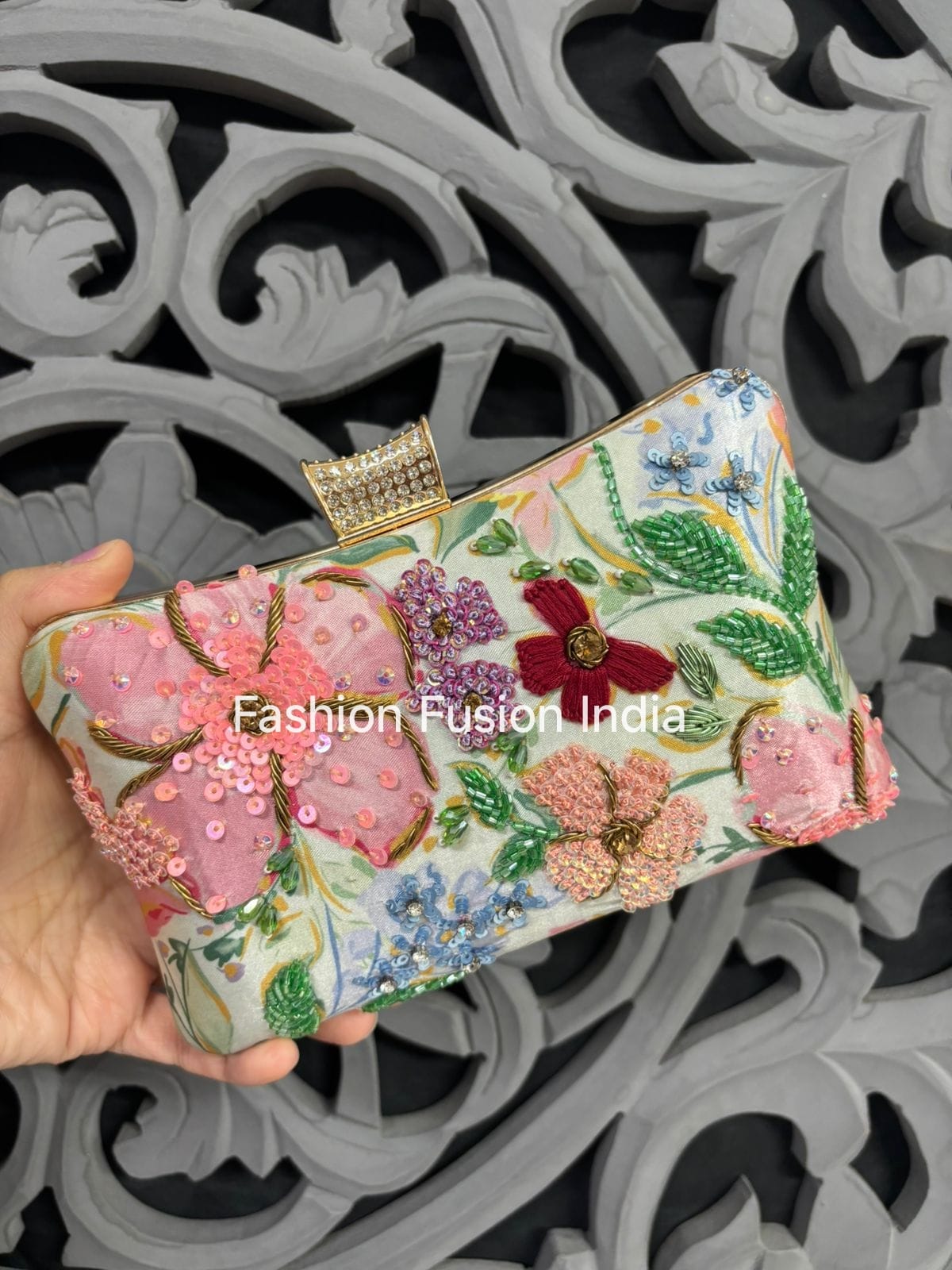 Floral embroidered clutch held by a hand with 'Fashion Fusion India' branding.