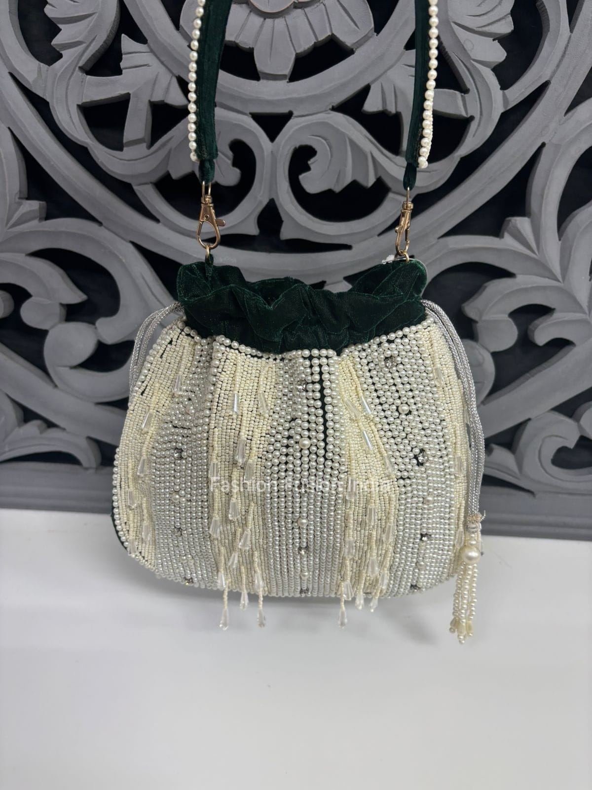 Decorative handbag with beads and fringes on a white surface with a decorative black and white background.