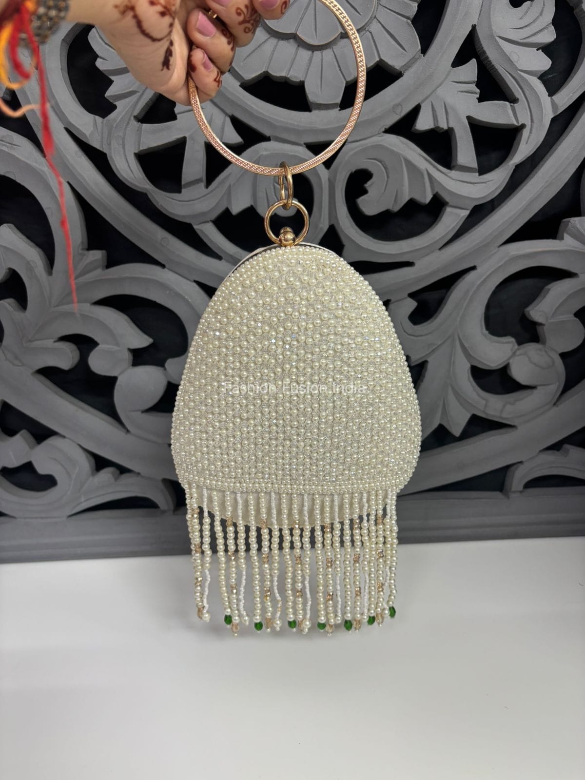 Beaded handbag with tassels held by a hand against an ornate wall.