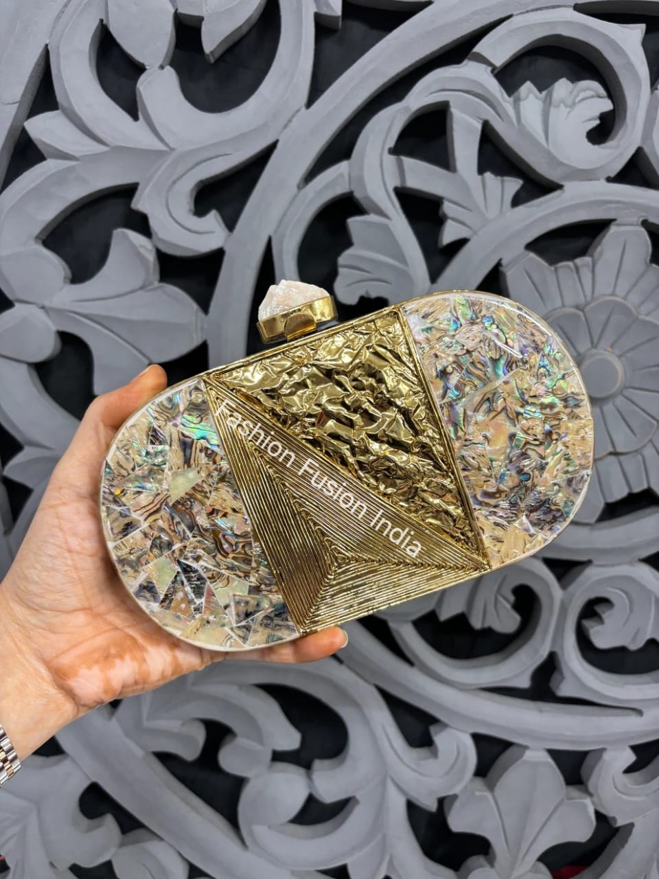 Decorative clutch held by a hand with 'Fashion Fusion India' branding against an ornate gray background.