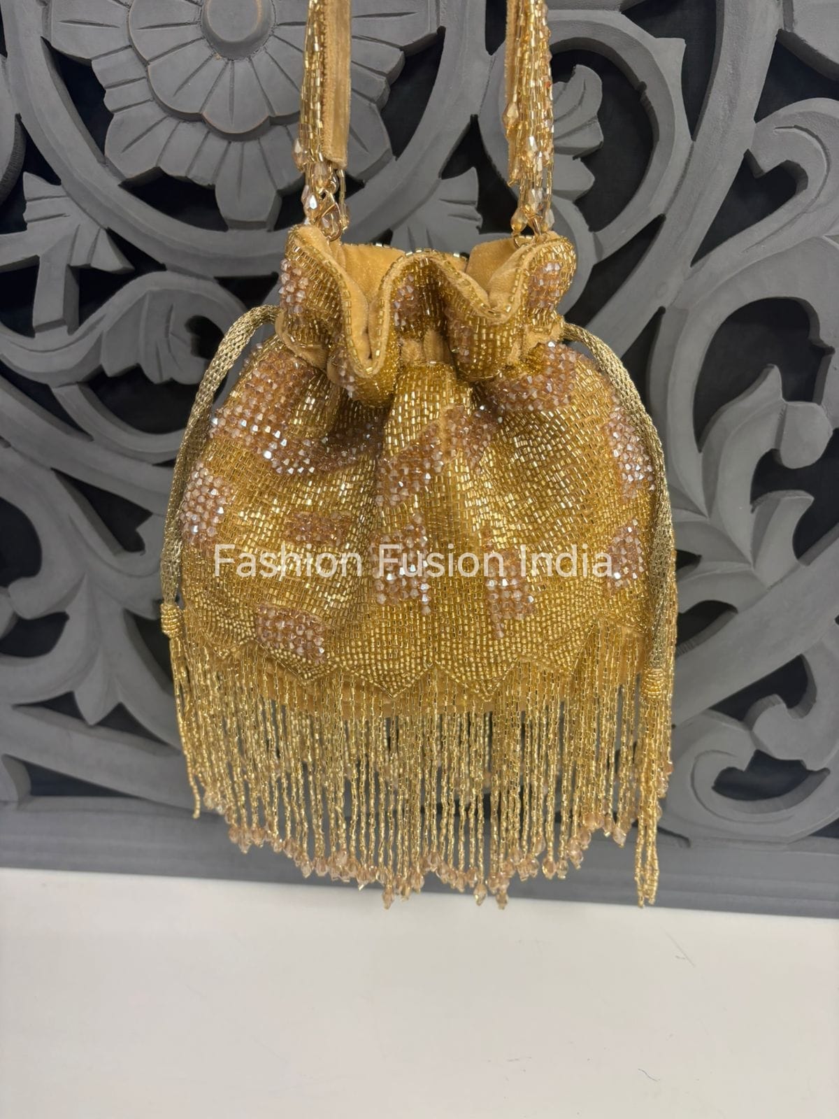 Gold beaded handbag with fringe against a decorative wall.