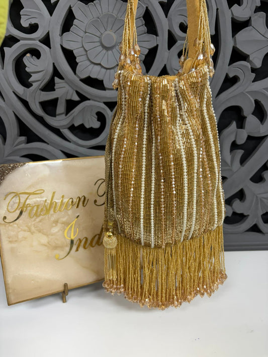 Gold beaded handbag with tassels on a white surface with decorative background