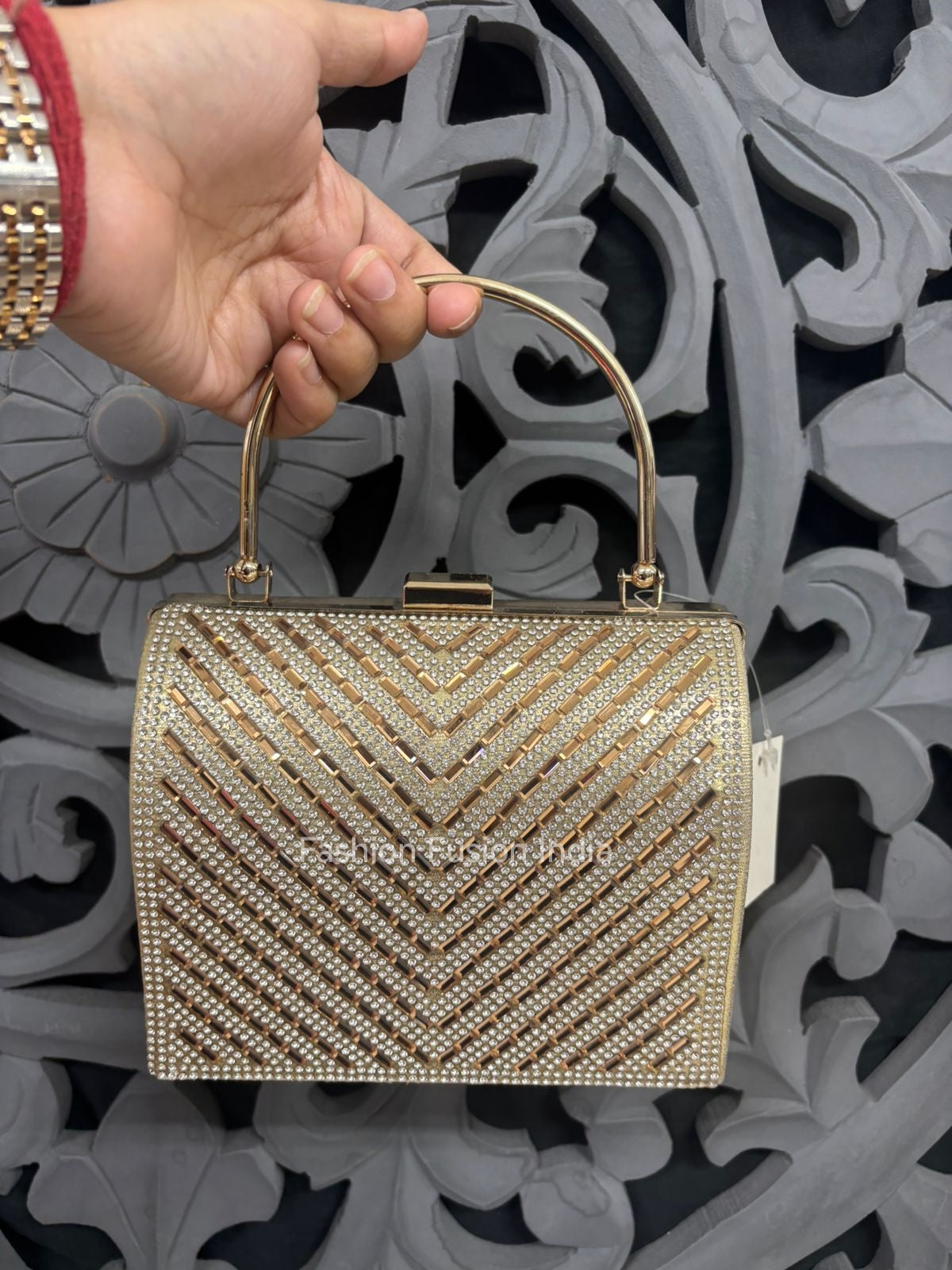 Gold handbag with intricate design held by a hand against an ornate background