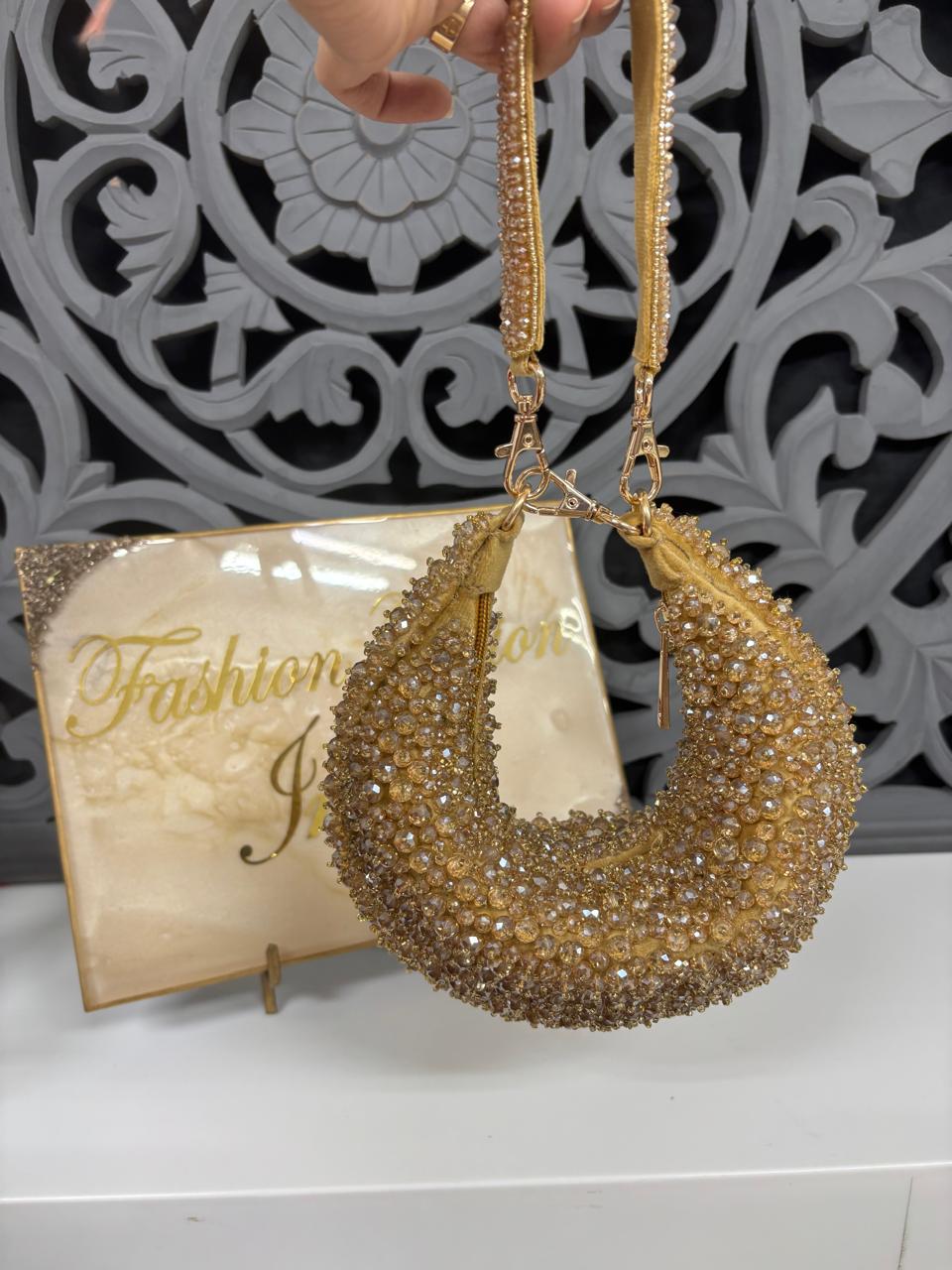 Gold beaded handbag held by a hand with a decorative background