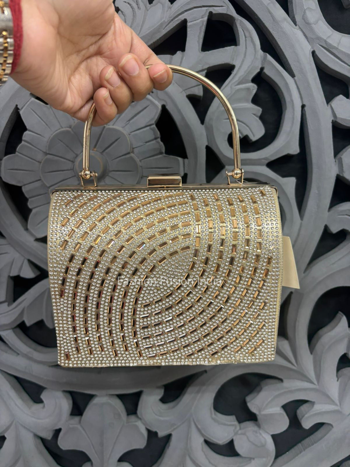 Gold beaded handbag held by a hand against an ornate gray background
