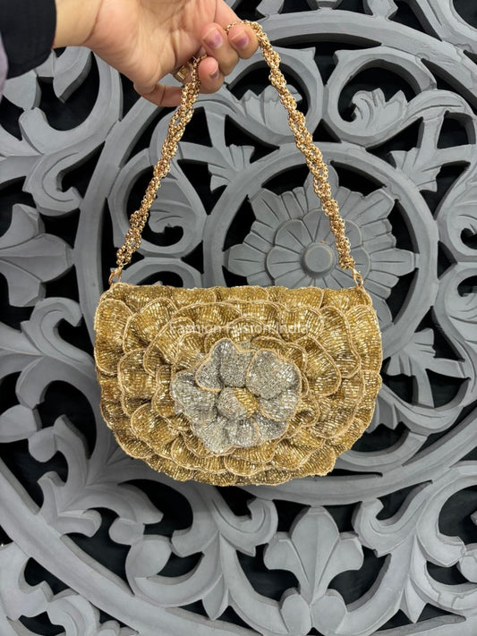 Gold handbag with floral design held by a hand against an ornate decorative background