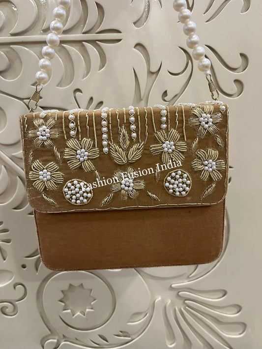 gold handbag with floral embroidery and pearl details on a decorative white background