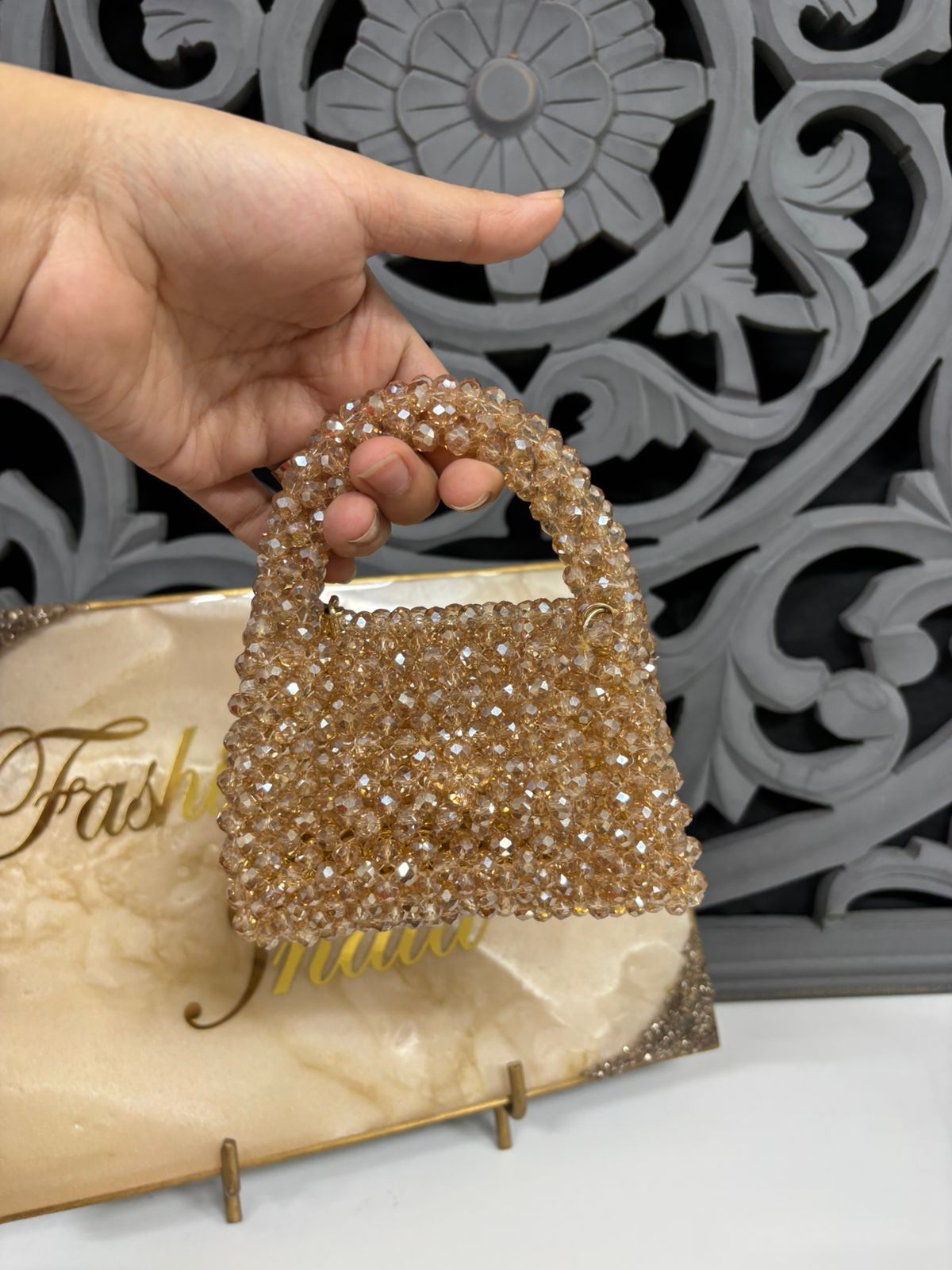 Gold beaded handbag held by a hand with a decorative background