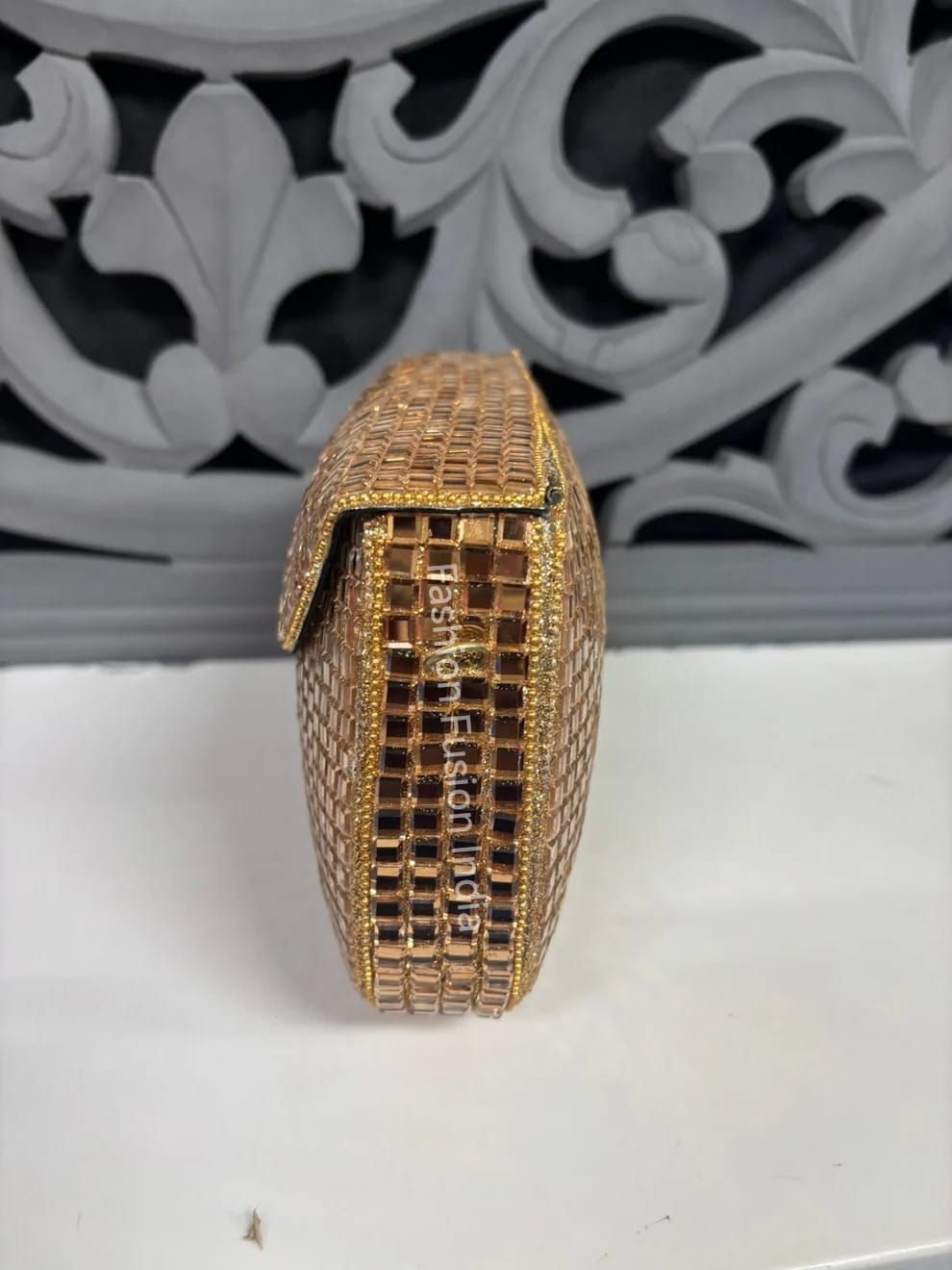 Gold clutch bag with intricate design on a white surface with decorative gray background