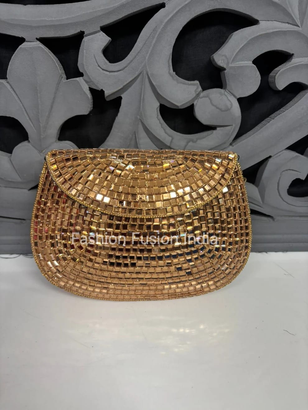 Gold beaded clutch bag on a white surface with decorative gray background