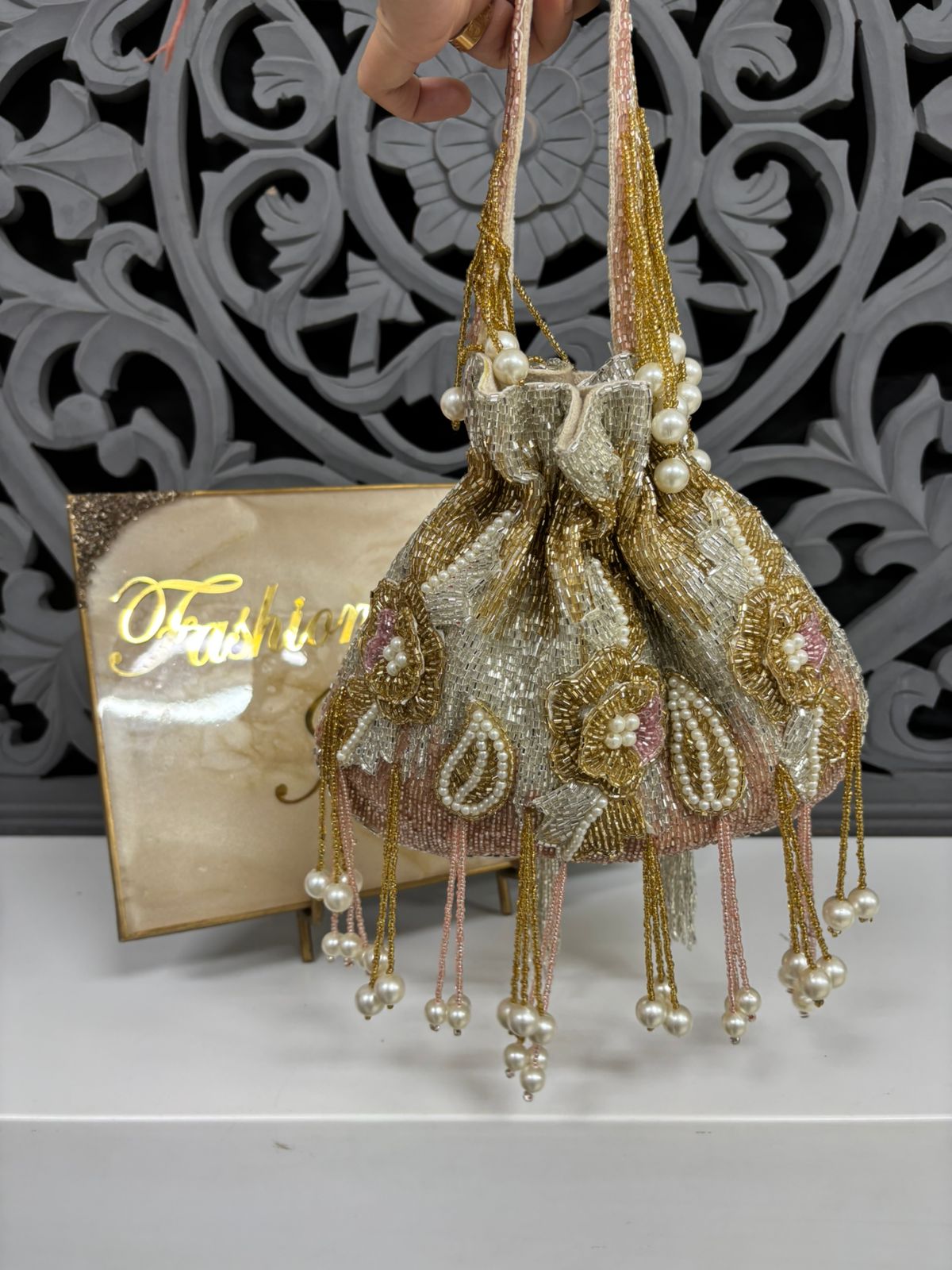 Decorative handbag with pearl details held by a hand against a decorative wall.
