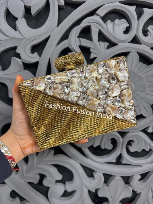 Gold clutch with decorative stones held by a hand against a decorative background, branded 'Fashion Fusion India'.