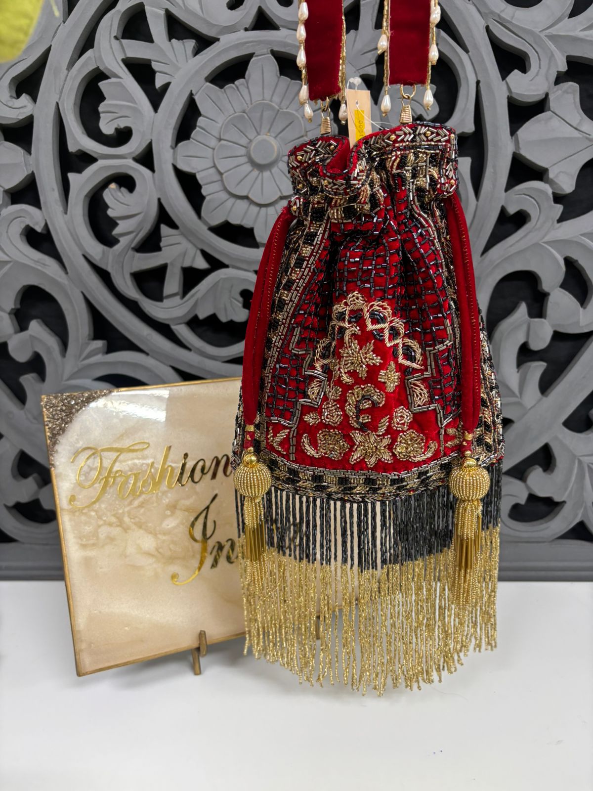 Decorative red and gold handbag with tassels on a white surface with a decorative gray background.
