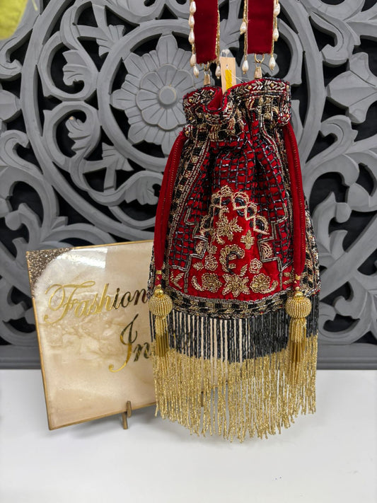 Decorative red and gold handbag with tassels on a white surface with a decorative gray background.