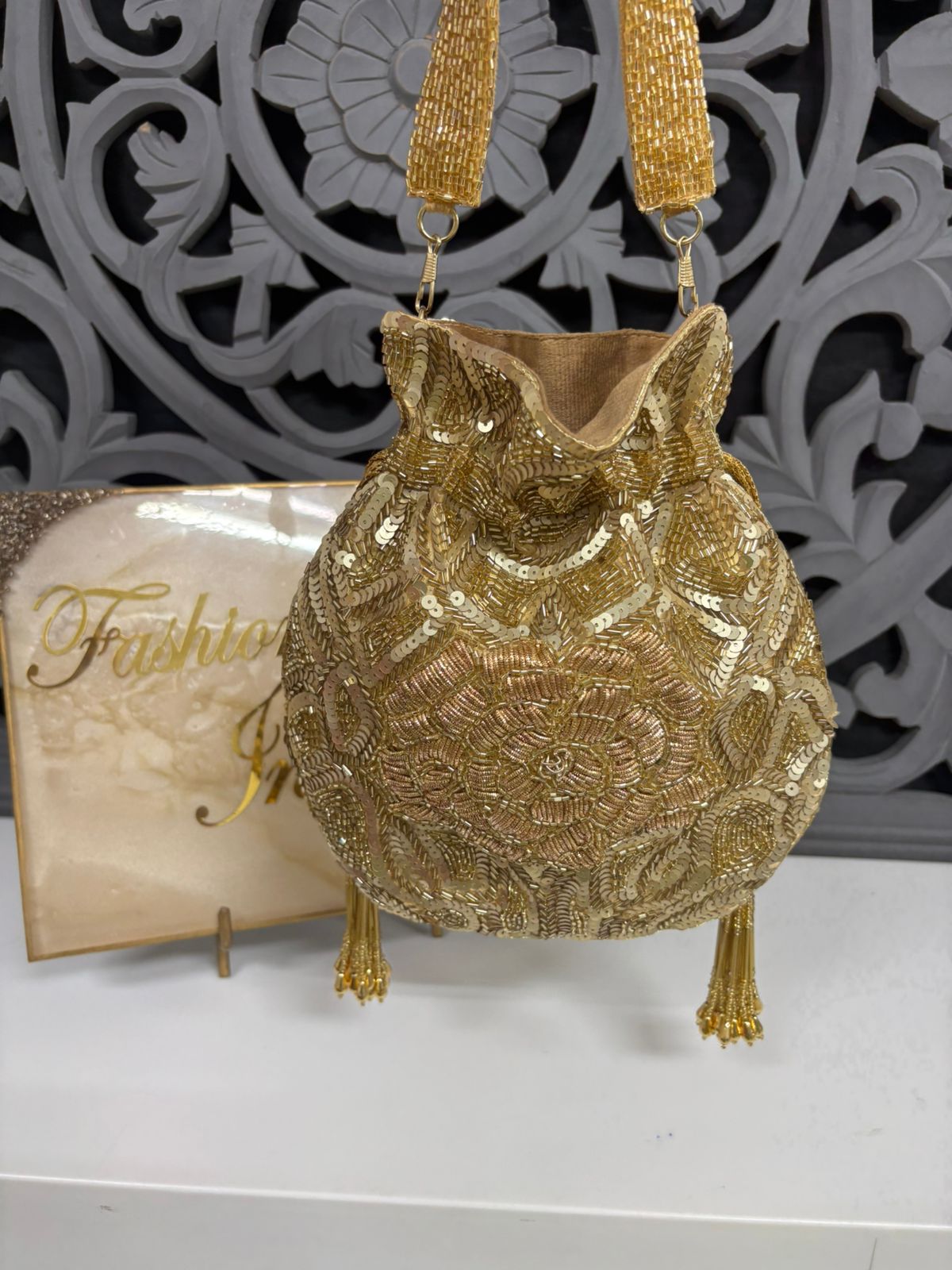 Gold beaded handbag with decorative design on a white surface, with 'Fashion' magazine in the background.