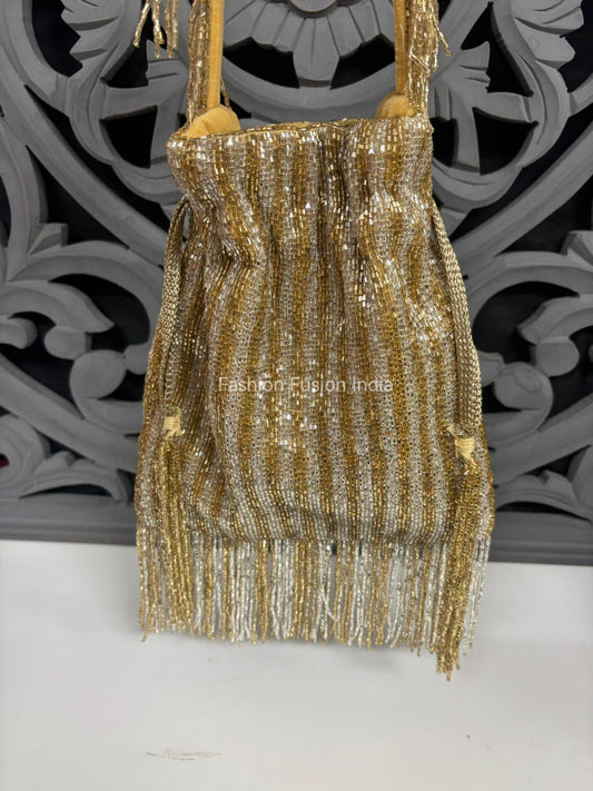 Gold aur silver beads se heavily embellished potli bag, vertical striped pattern ke saath, upar gathered design aur neeche fringe tassels. 