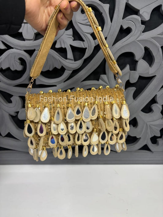 Gold handbag with decorative elements held by a hand against an ornate background