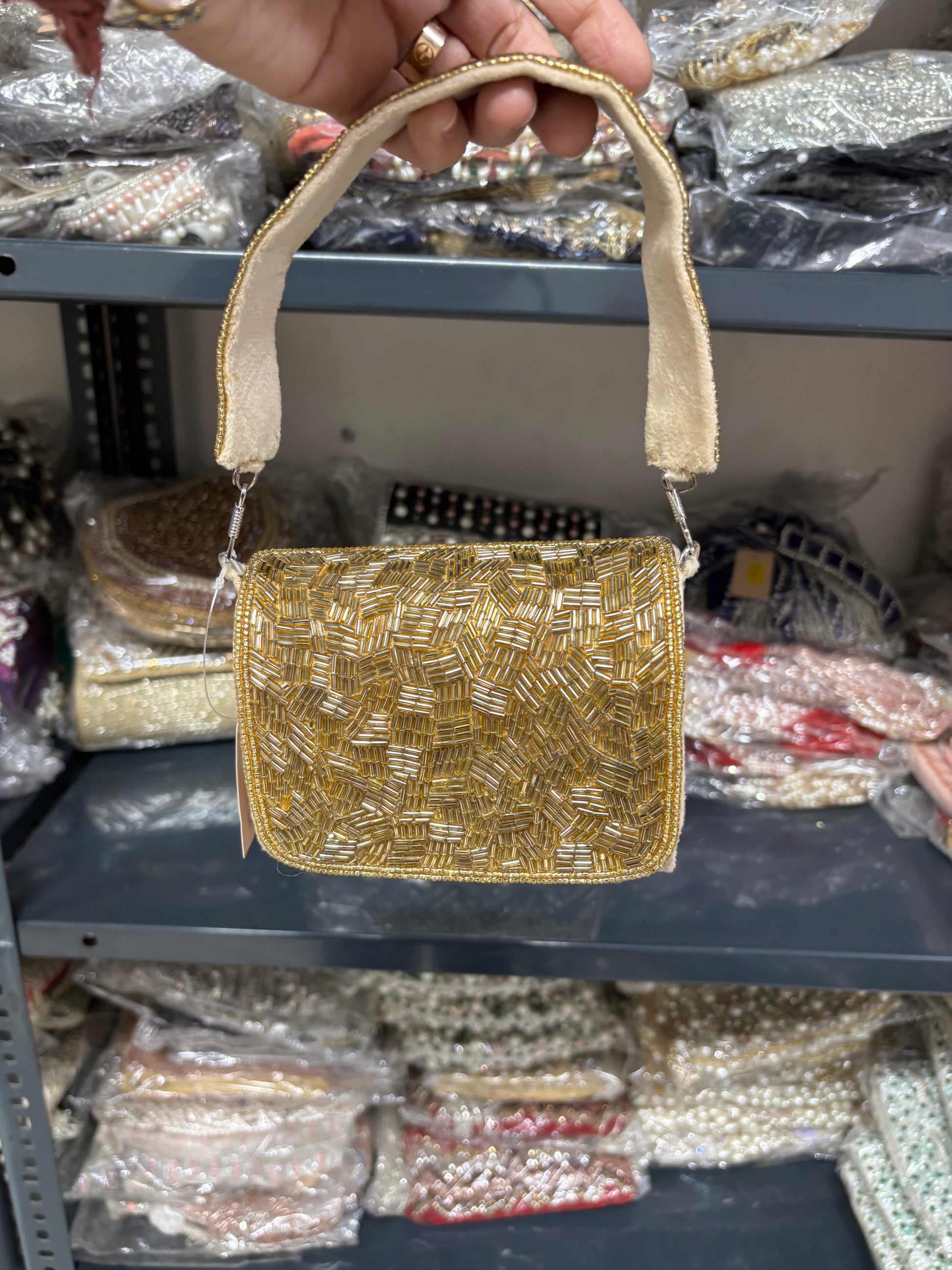 Gold beaded handbag held by a hand with a blurred store shelf in the background