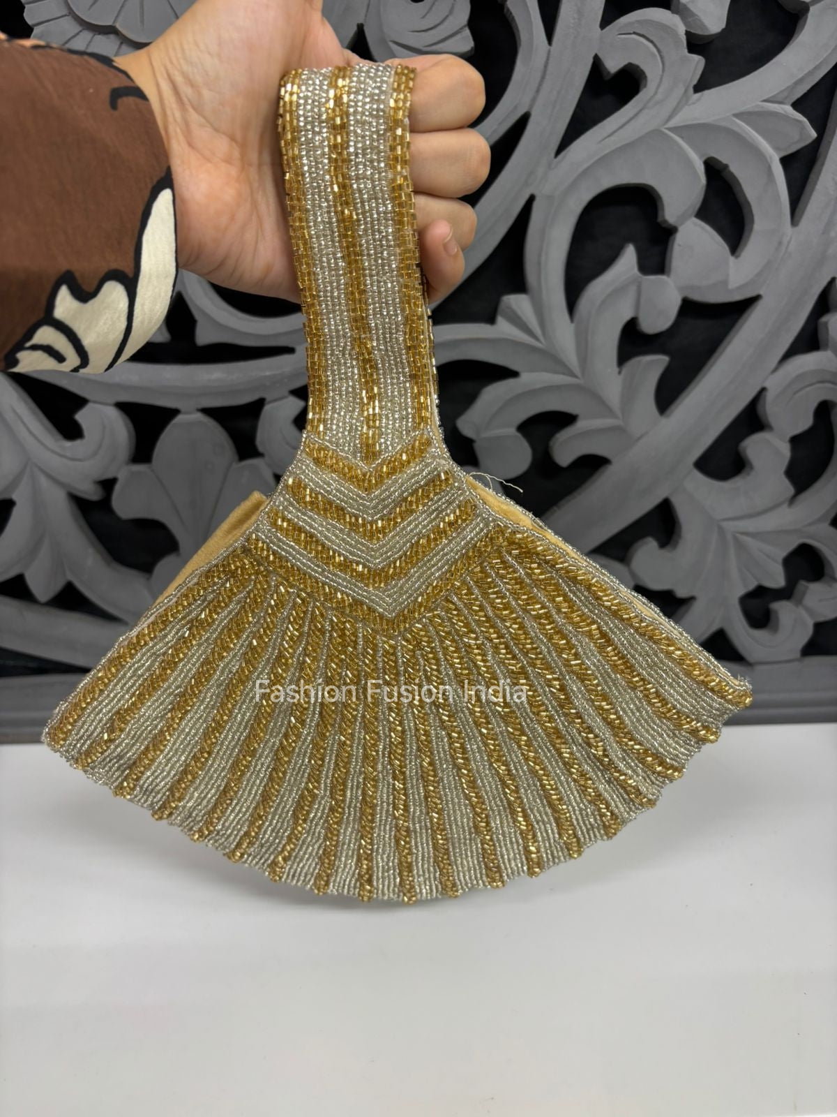 Gold and silver beaded clutch held by a hand with a decorative background