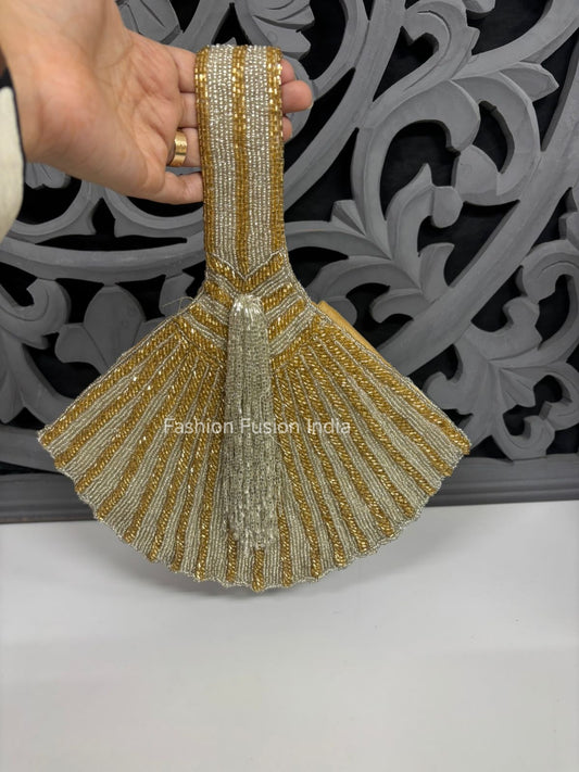 Decorative handbag with gold and white beading held by a hand against a decorative gray background.