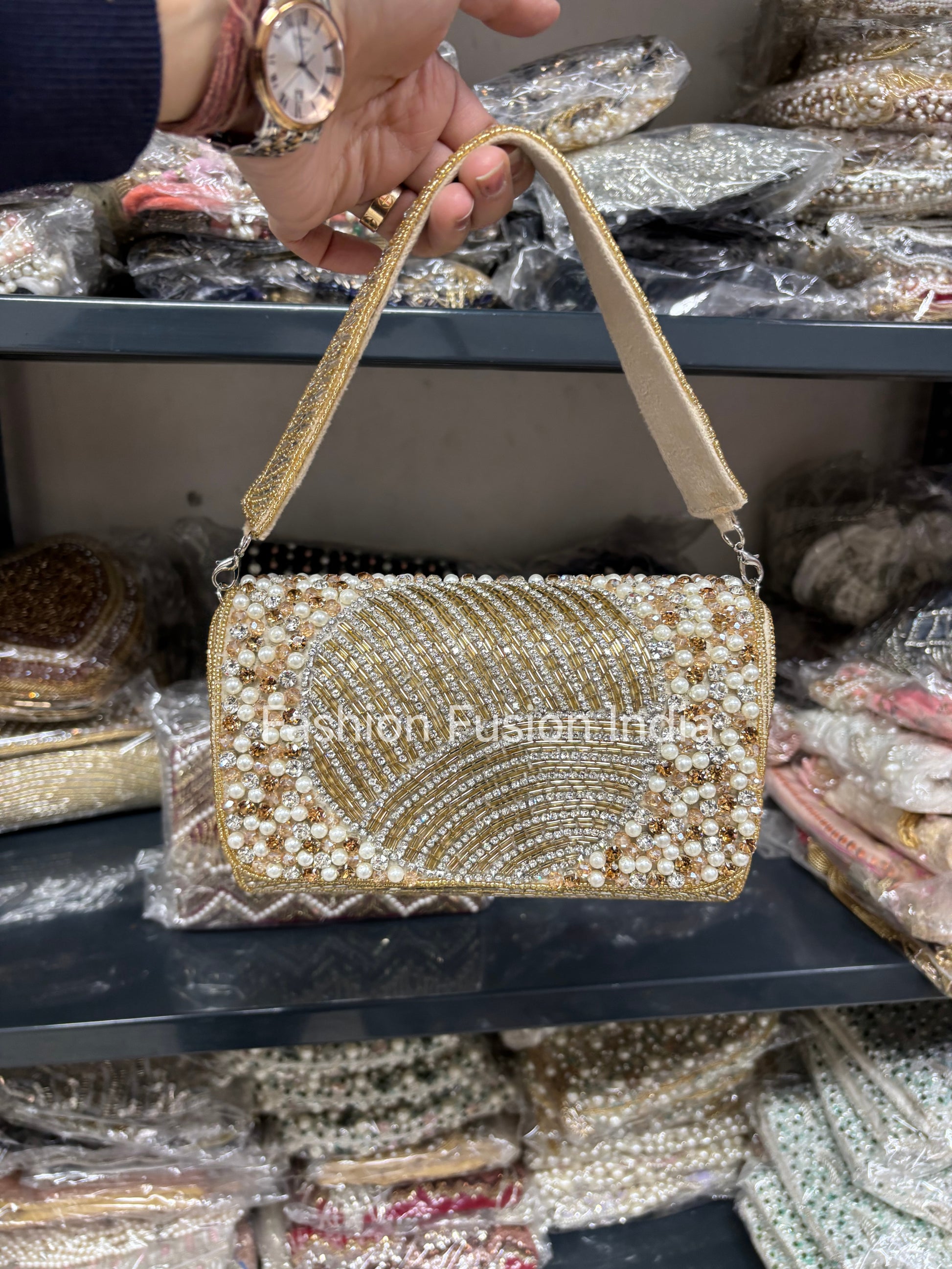 Gold beaded handbag held by a hand with a watch, against a background of similar bags.