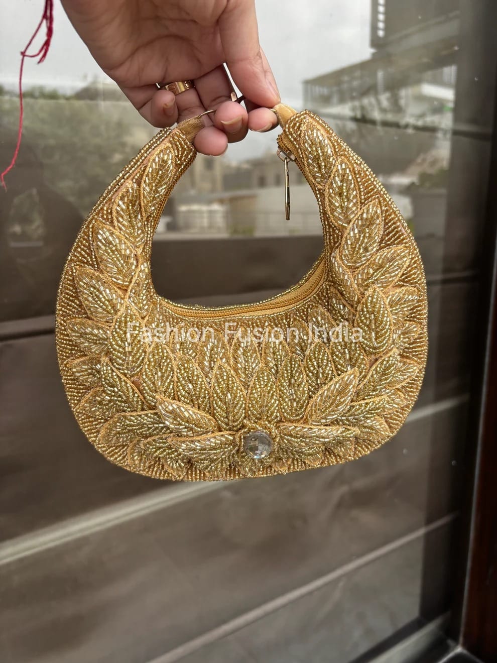 Gold embroidered handbag held by a hand with a blurred background