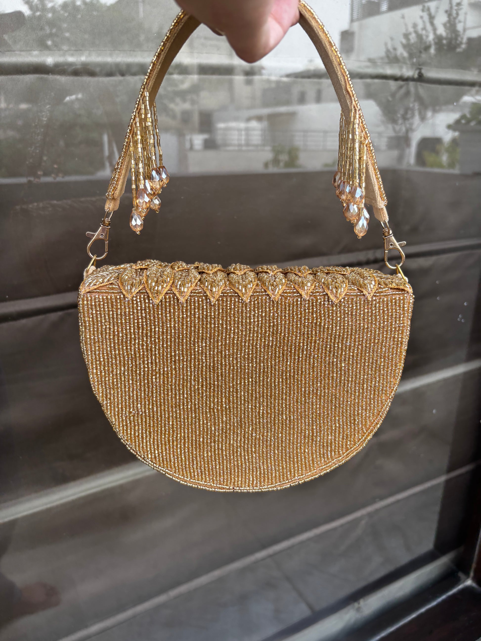 Gold beaded handbag with tassels held by a hand against a blurred background