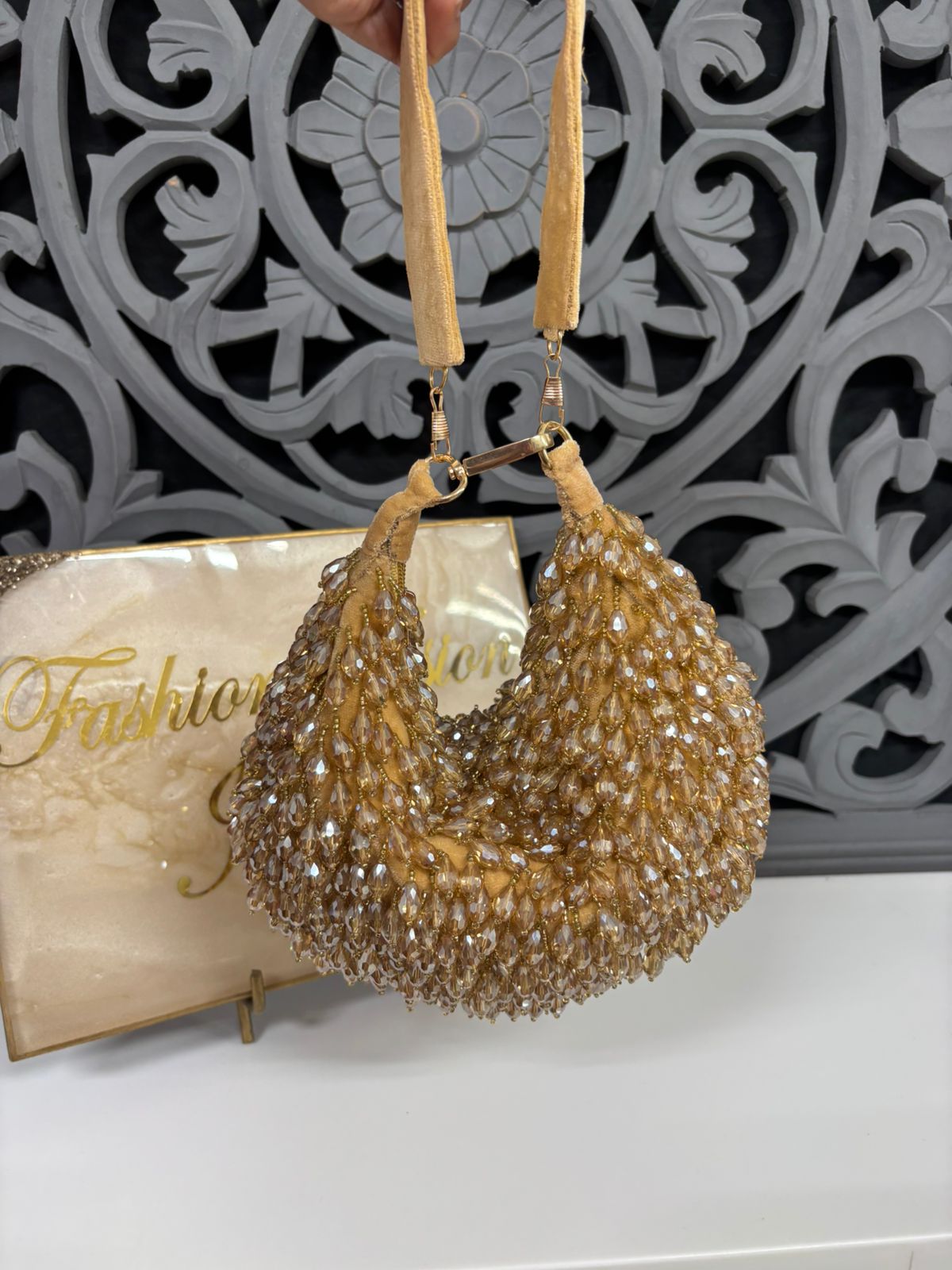 Gold beaded handbag held by a hand with a decorative background