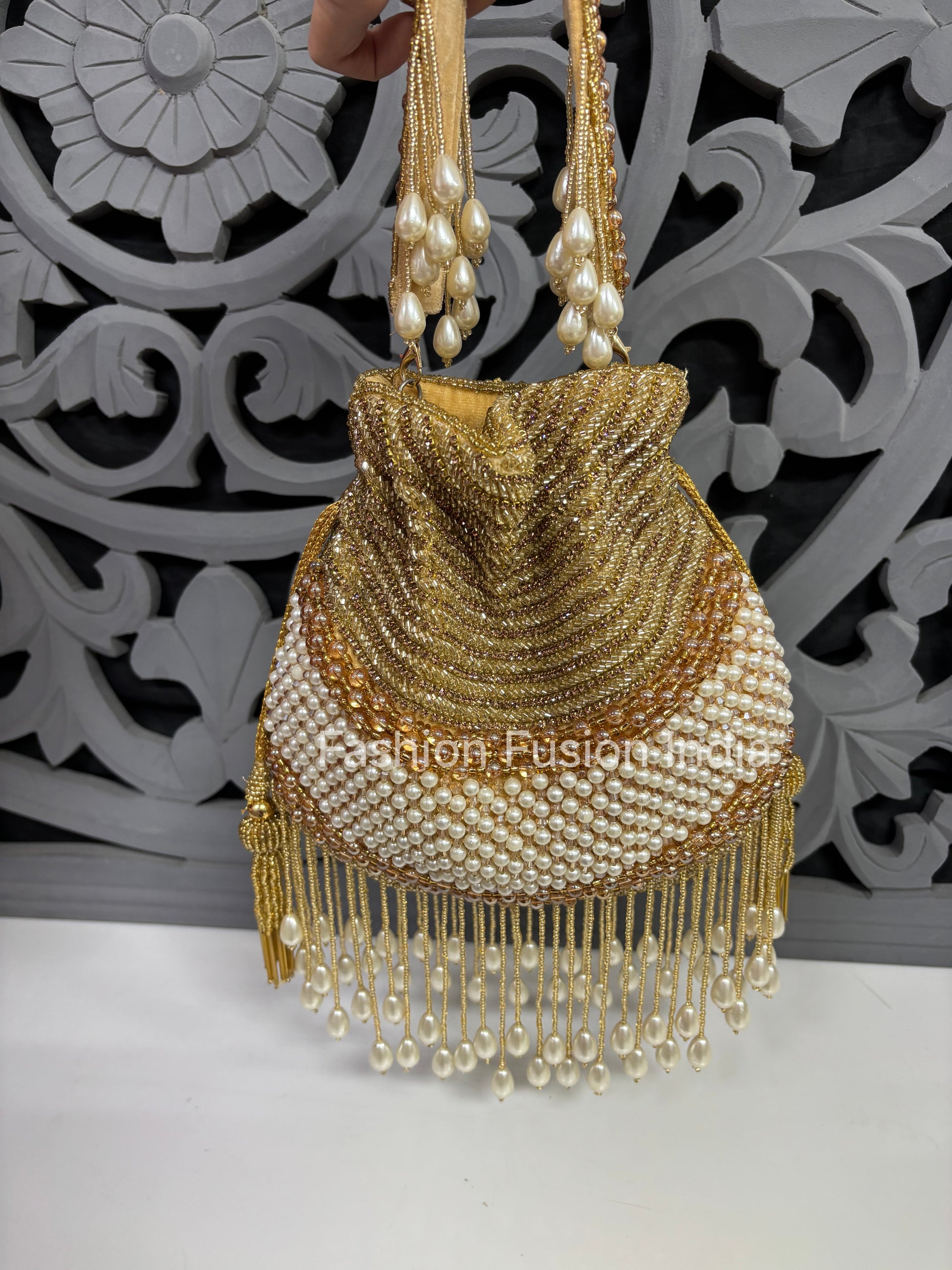 Gold beaded handbag with pearl details against a decorative white and black background