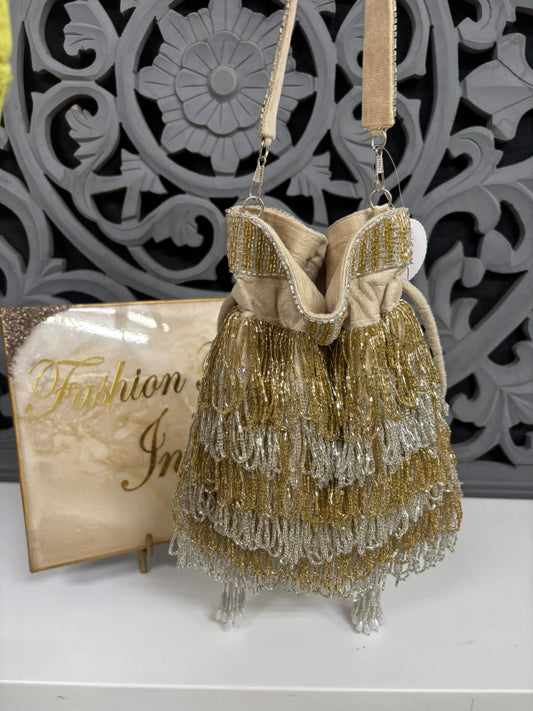 Gold beaded handbag with decorative strap on a white surface, with 'Fashion In' sign in the background.