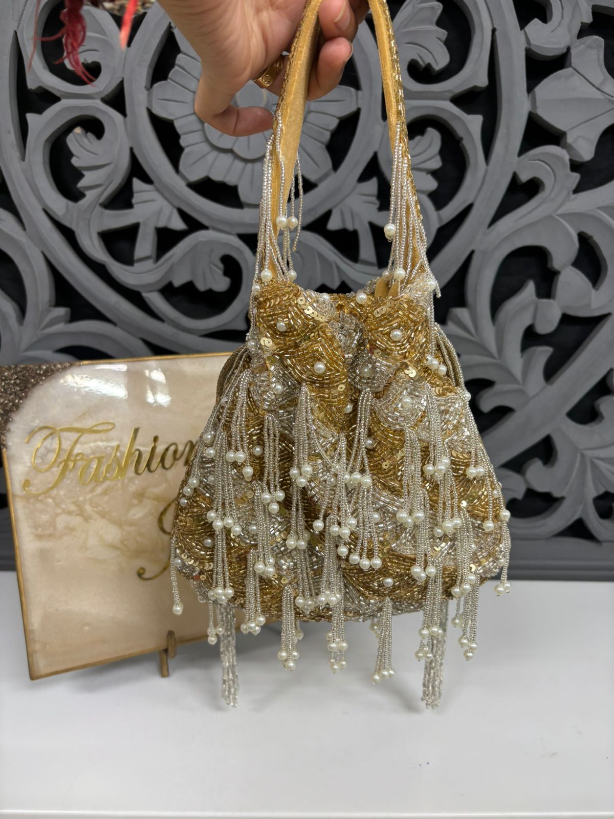 Gold beaded handbag with tassels held by a hand against a decorative background.