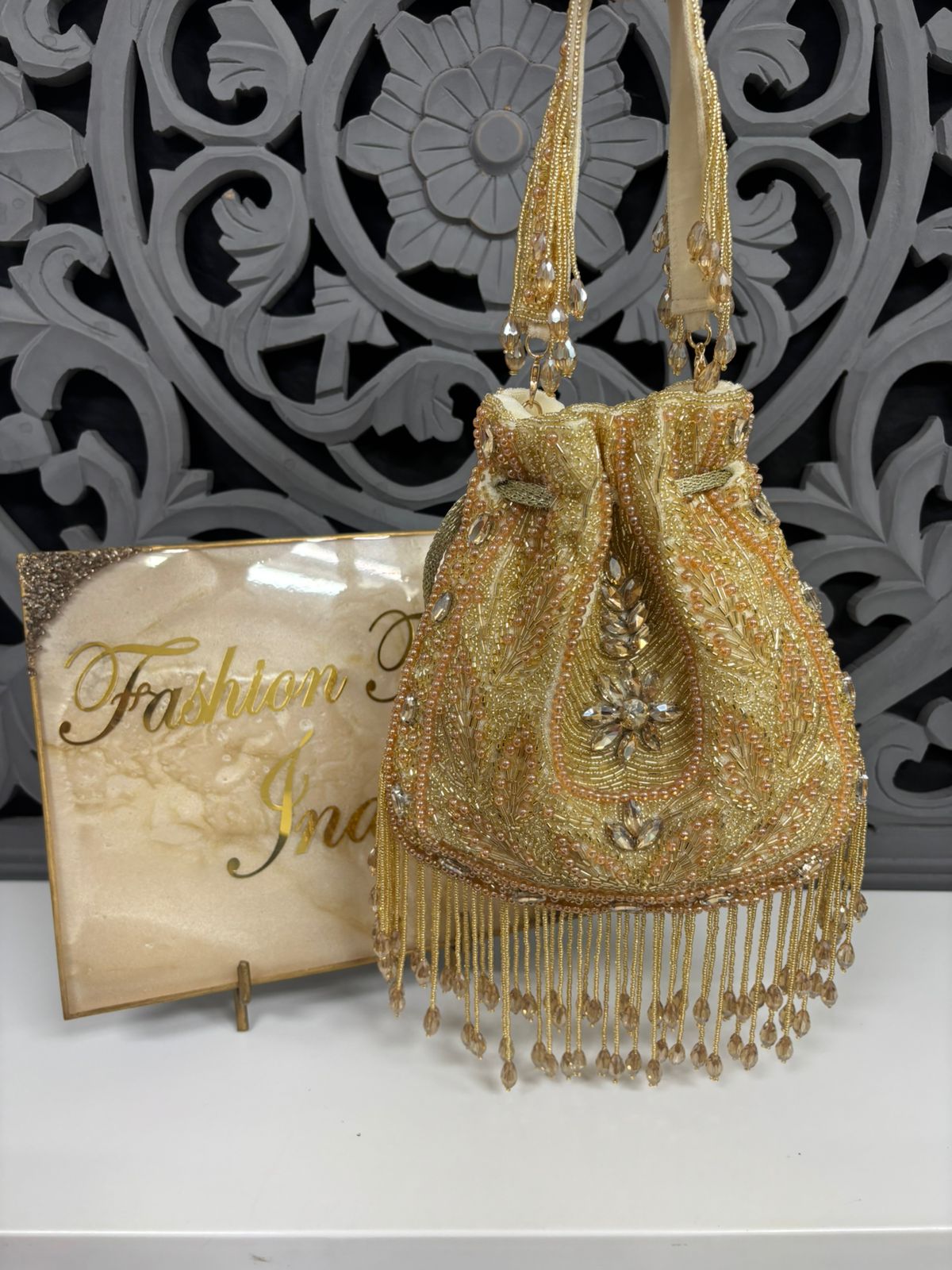 Gold beaded handbag with fringe details on a decorative background