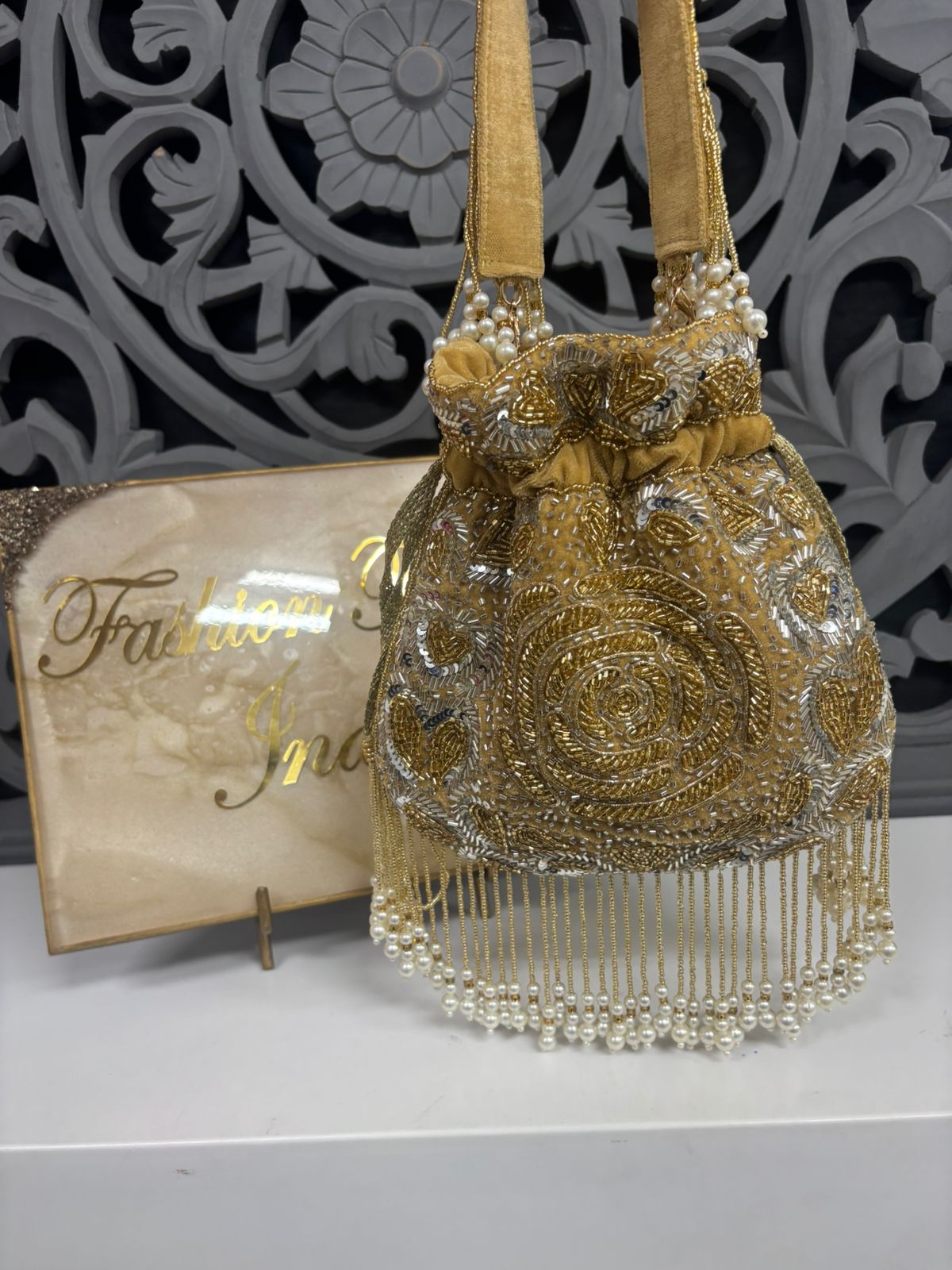 Gold beaded handbag with decorative patterns on a gray surface, with a decorative background.