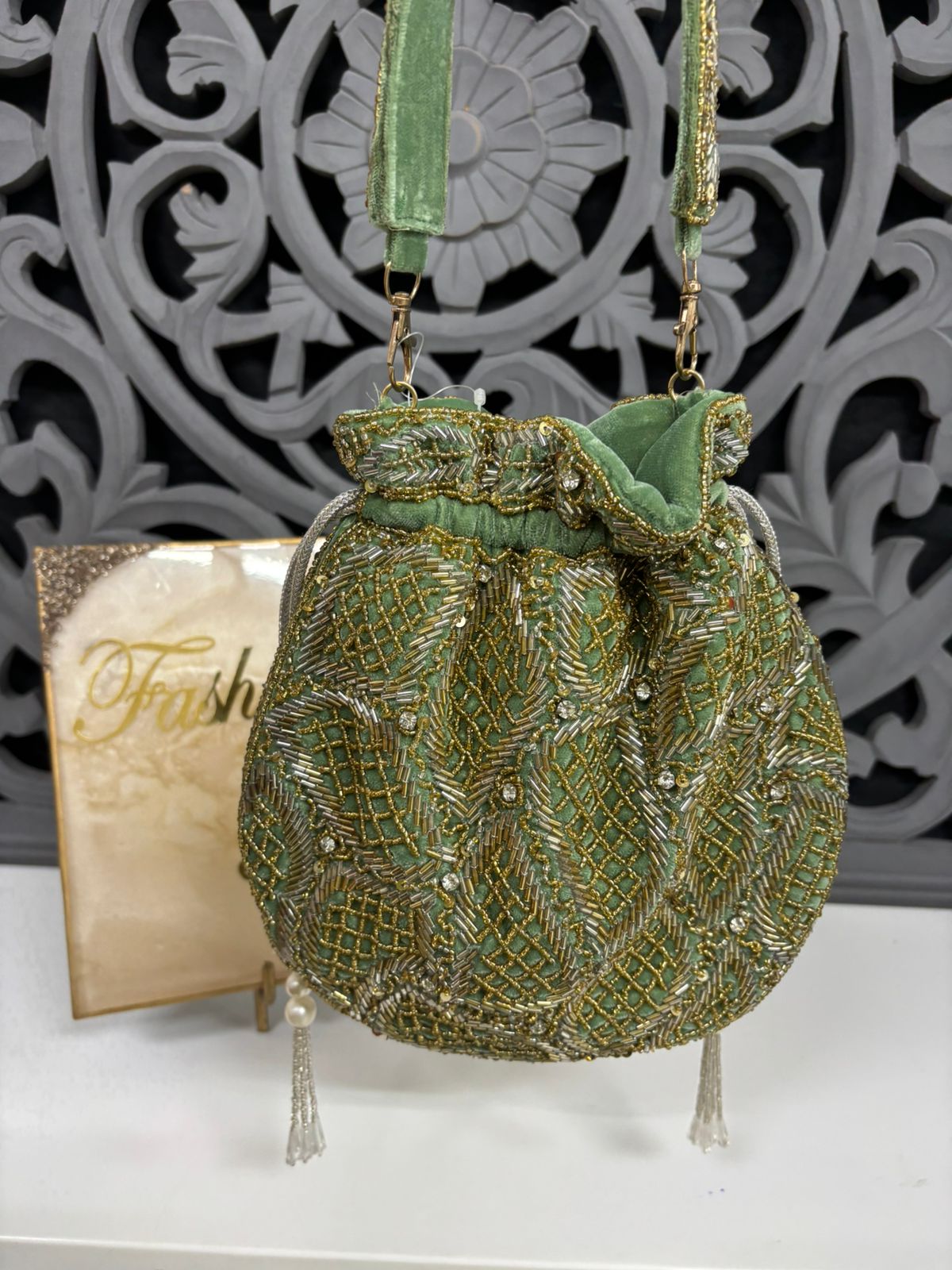 Green beaded handbag with decorative strap against a decorative metal background