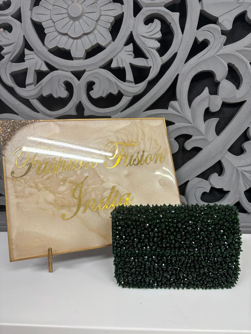 Green beaded clutch bag on a stand with 'Fashion Fritton India' branding against an ornate wall.