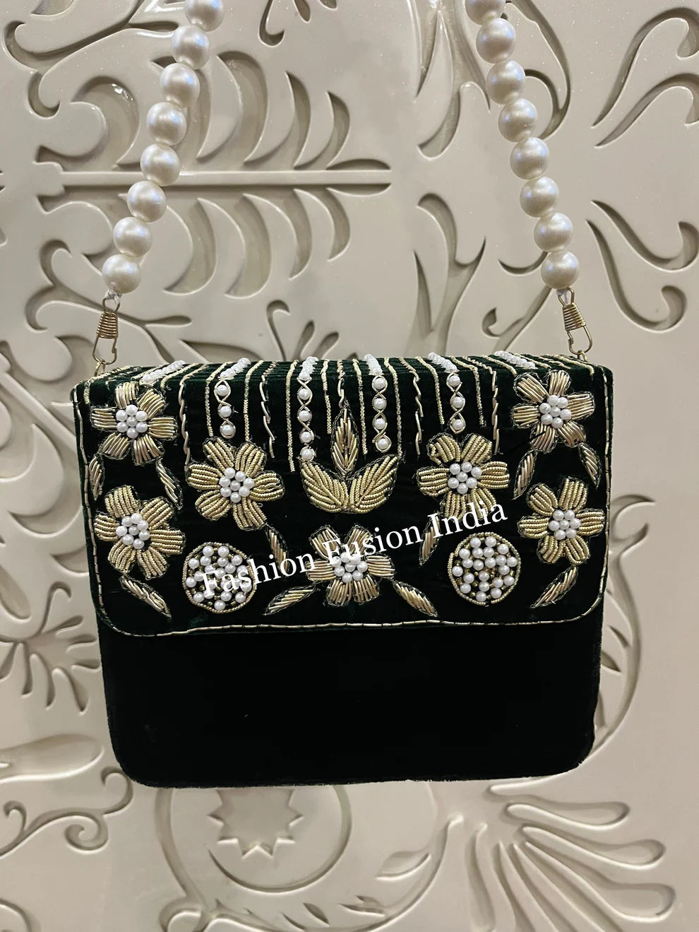 Green handbag with floral and pearl designs on a decorative white background