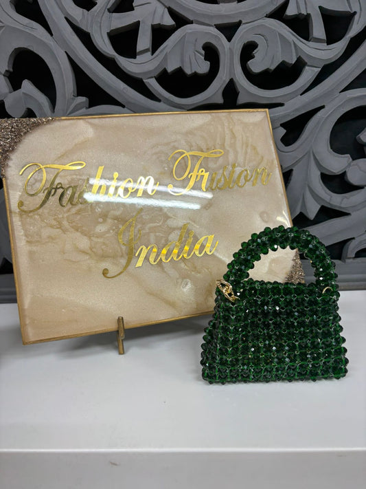 Green beaded handbag in front of a decorative sign with 'Fashion Trunk India' on a white surface.