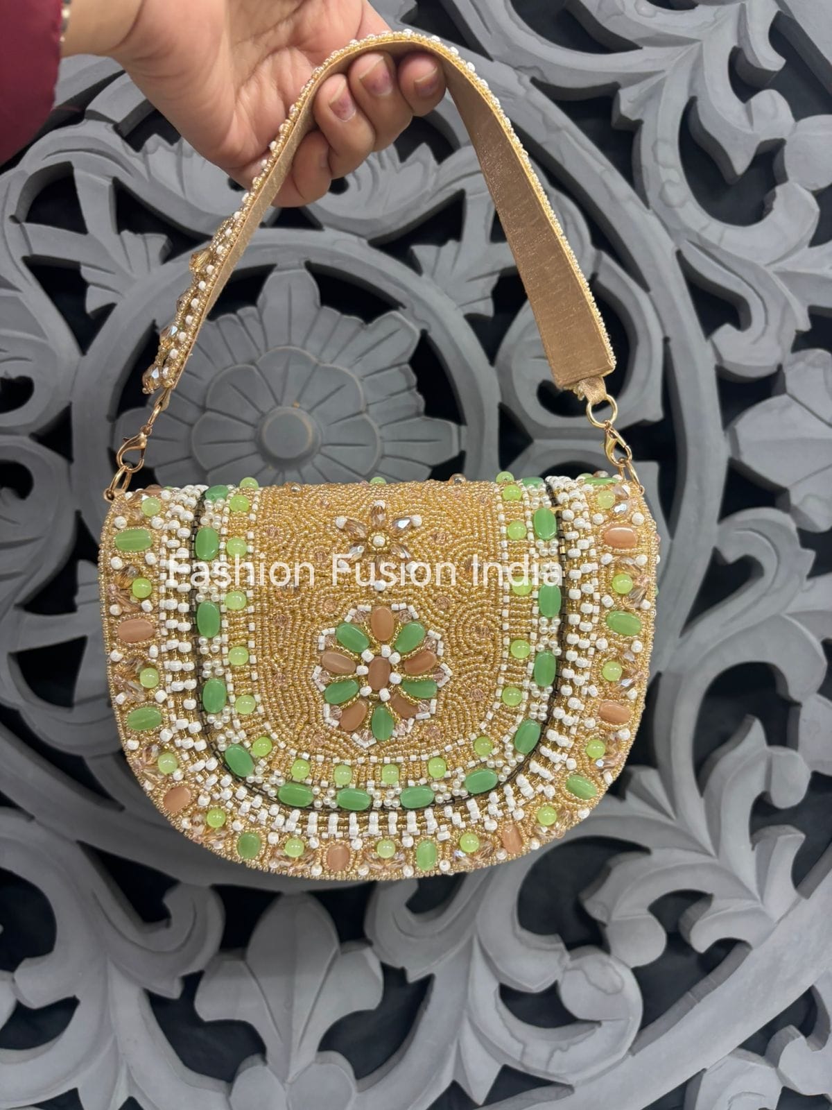 Decorative handbag with green and gold patterns held by a hand against an ornate background.